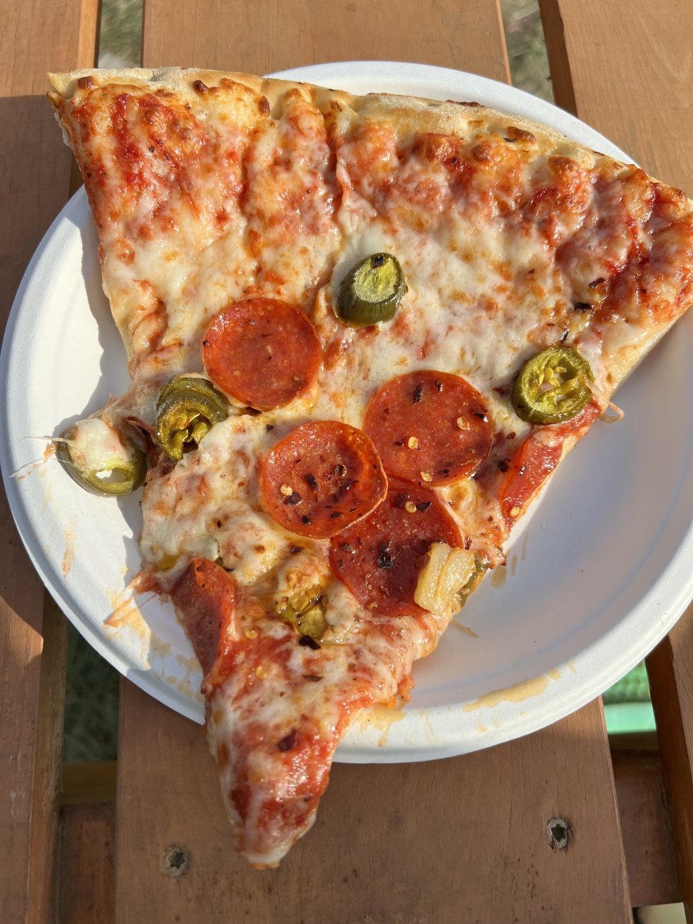 A big slice of pepperoni pizza with jalapeño on it