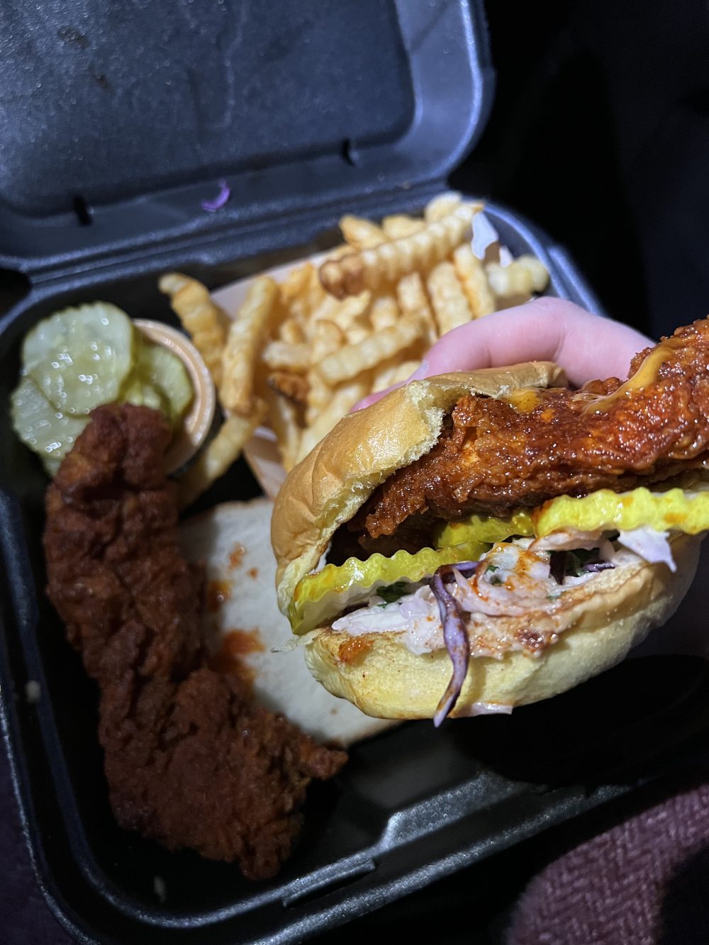 A box filled with Dave's hot chicken tenders, a sandwich, some pickles, and fries