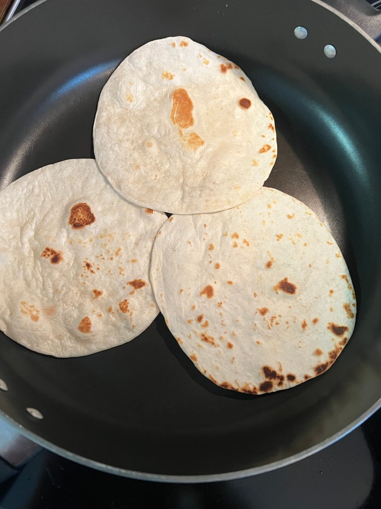 Flour tortillas toasting in a skillet on the stove