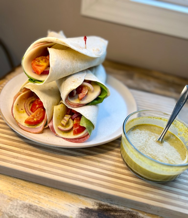 A plate of Italian Wraps on a wooden table with a dish of Italian Dressing nearby