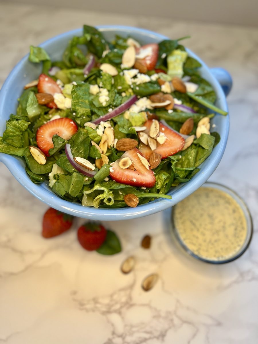 A strawberry salad in a blue bowl with lemon poppy seed dressing nearby on a marble counter