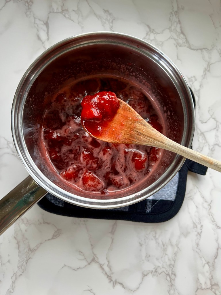 Strawberry compote in a saucepan on a hot pad on a marble counter