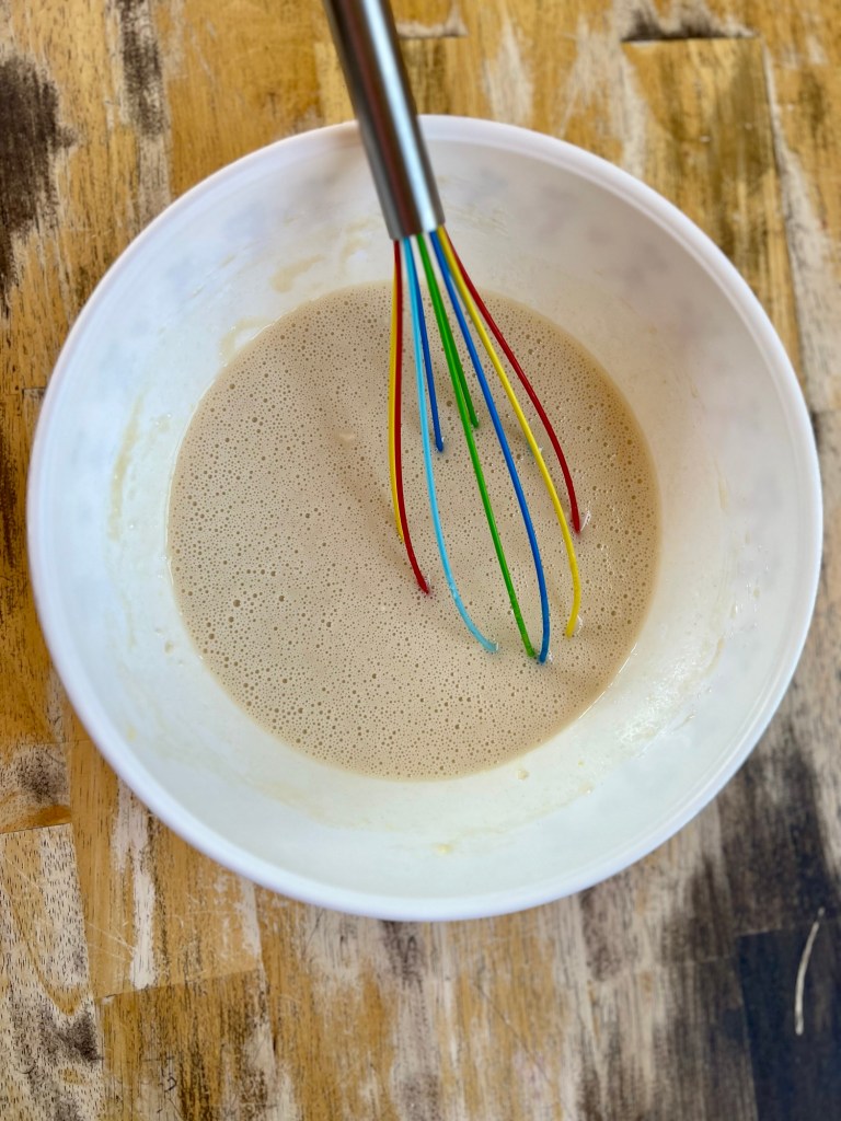 A mixing bowl filled with cobbler batter with a whisk inside