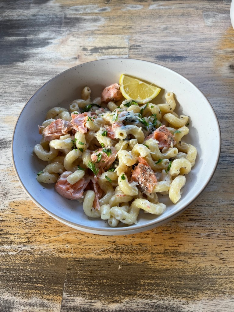 Creamy Salmon Pasta in a white bowl with parsley and lemon wedges for garnish on a wooden table