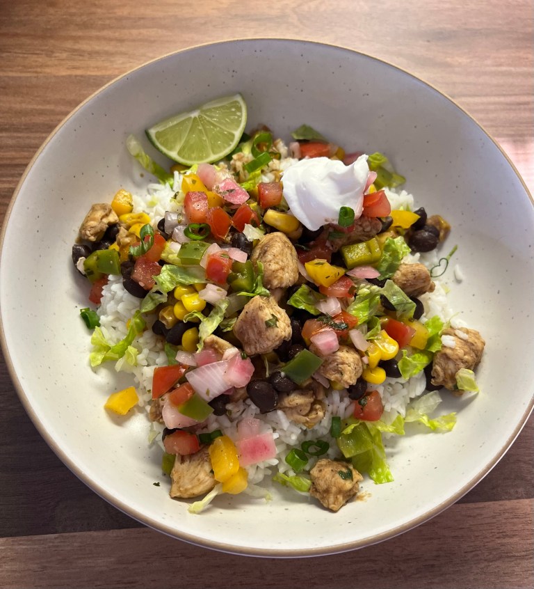 Chicken Burrito Bowl in a white bowl with sour cream, herbs, and lime for garnish