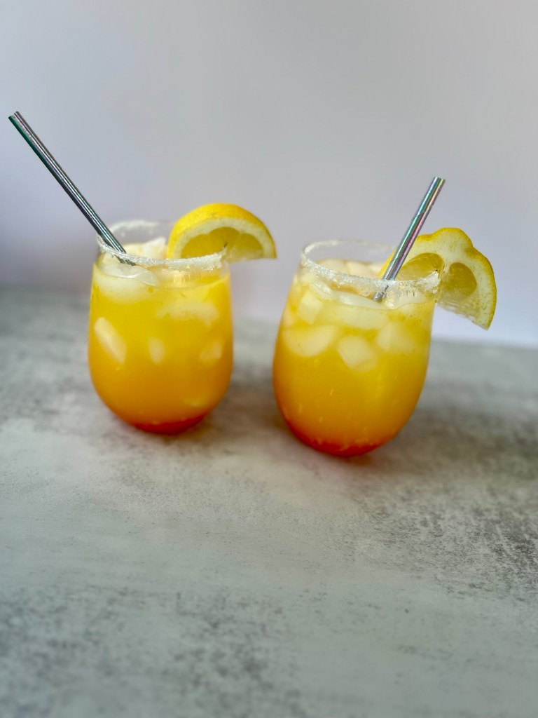 Two vodka summer sunrise drinks with lemon wedges for garnish and straws sitting on a countertop