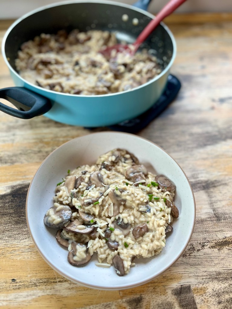 Mushroom Risotto in a large skillet with a white bowl of it next to it on a table