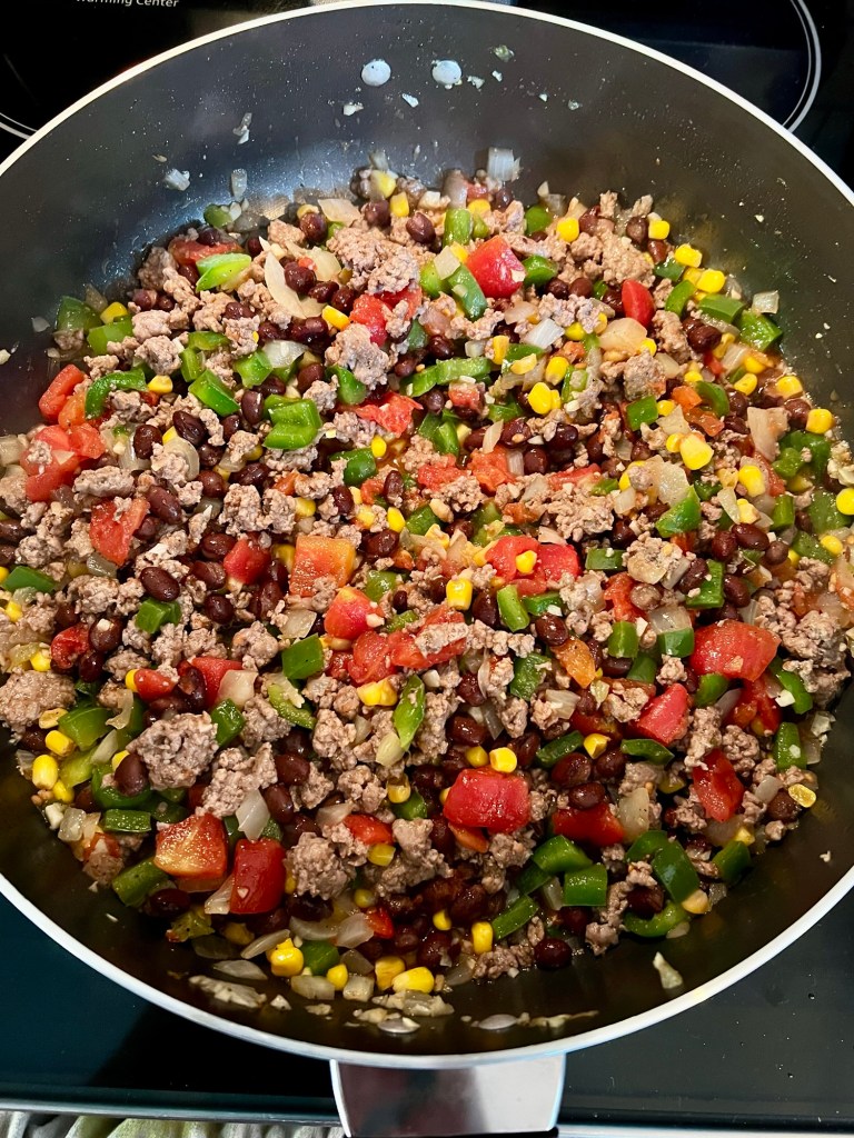 A large skillet on the stove filled with southwest burrito ingredients