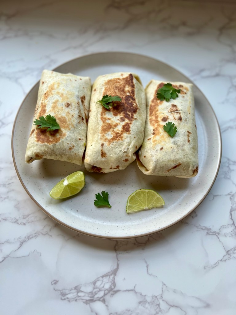 Three southwest burritos on a white plate with cilantro and lime garnish