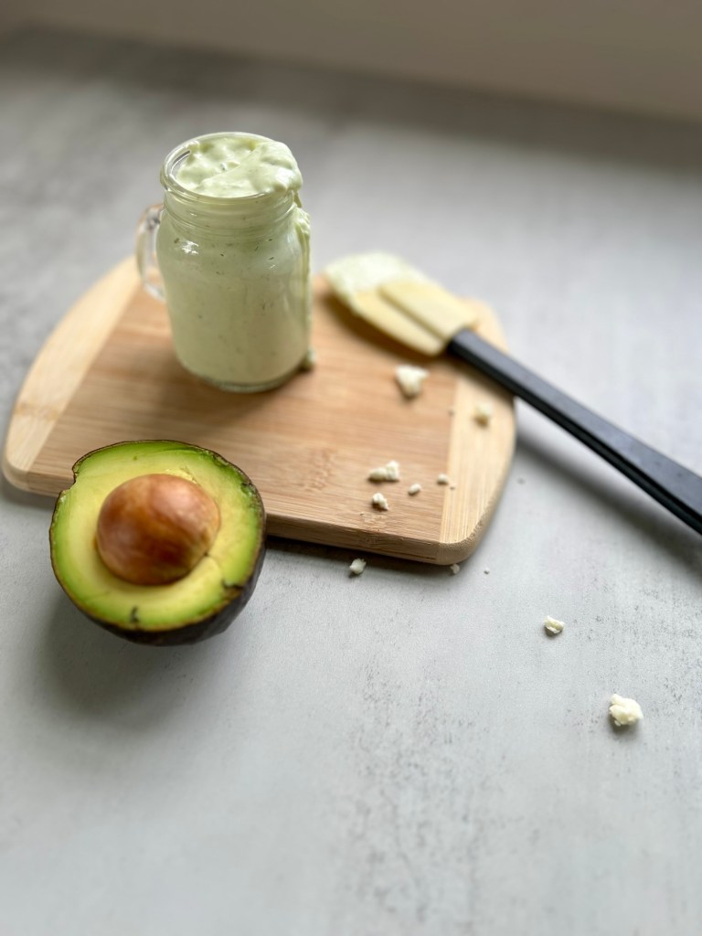 Avocado Blue Cheese Dressing in a glass dish with an avocado and rubber spatula nearby
