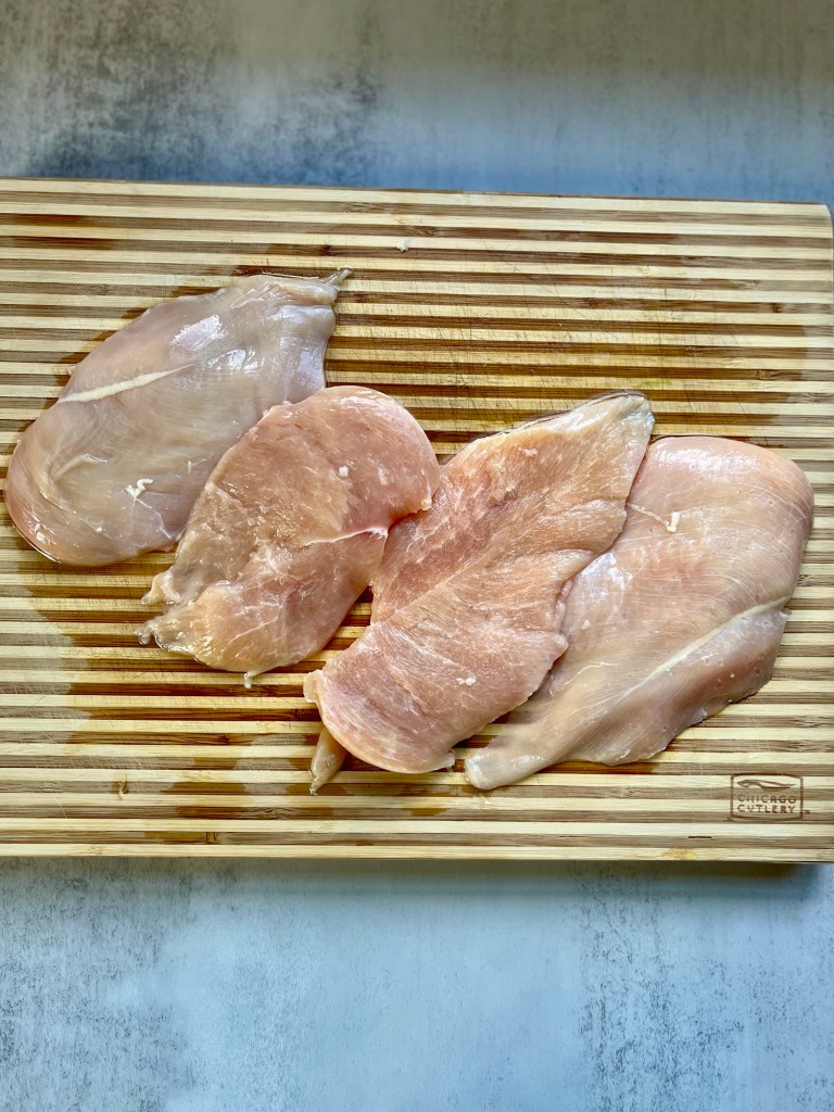 Chicken breasts that have been cut in half on a wooden cutting board