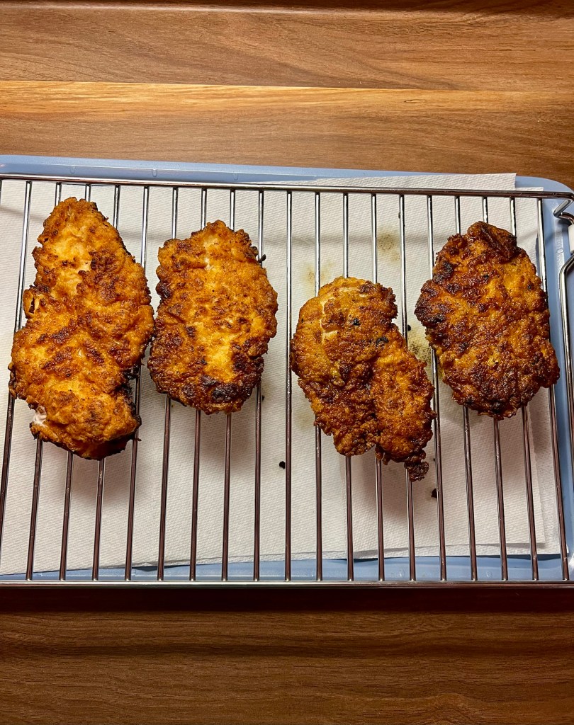 Fried chicken breasts on a rack with some paper towel underneath
