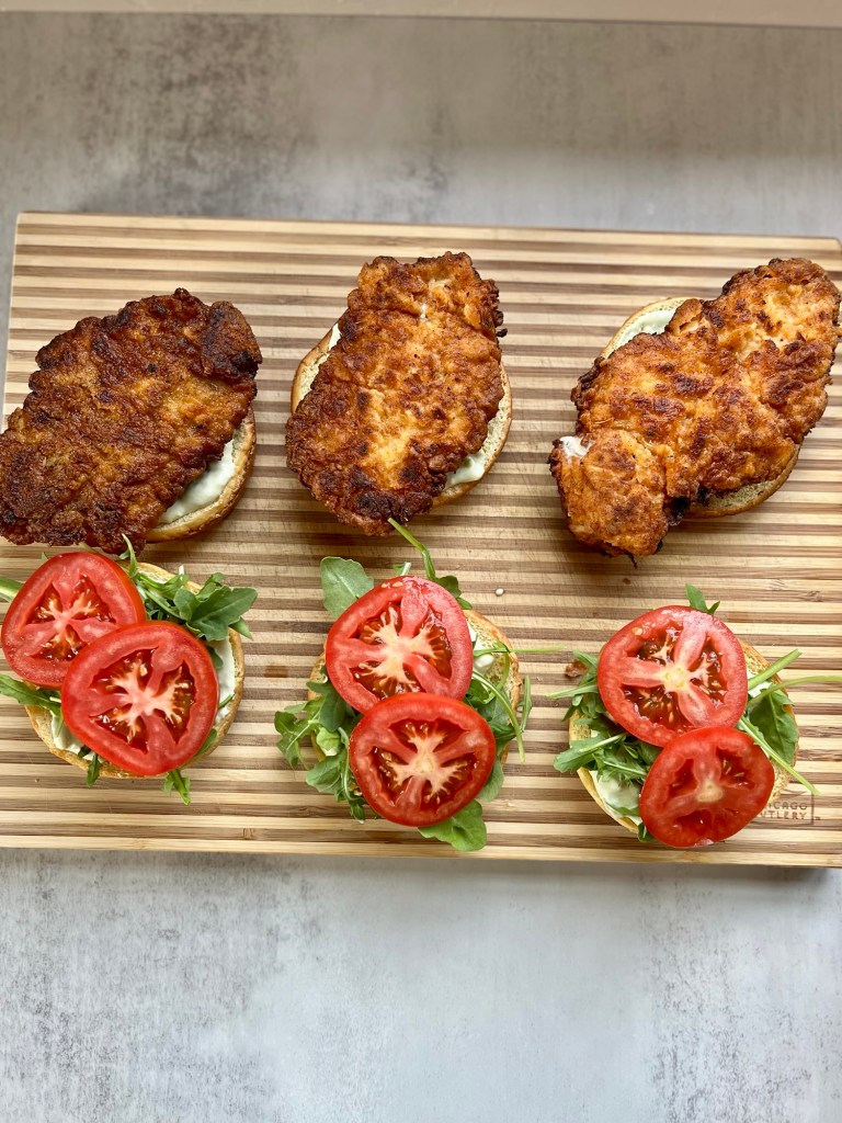 Spicy fried chicken sandwiches being assembled on a wood cutting board
