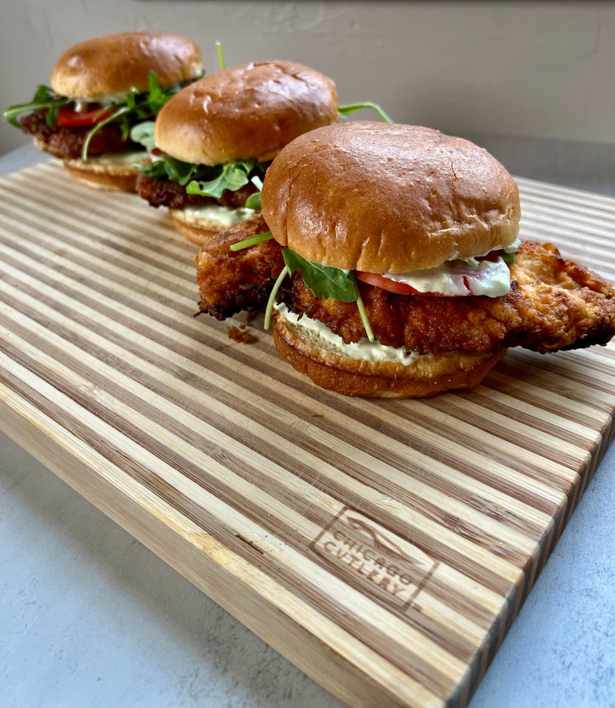 Three spicy fried chicken sandwiches on a wooden cutting board