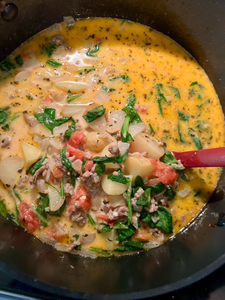 A large pot of creamy sausage and potato soup with a red serving spoon inside