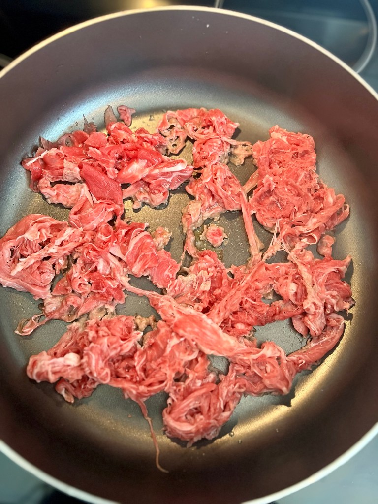 Shaved steak cooking in a large skillet on the stove