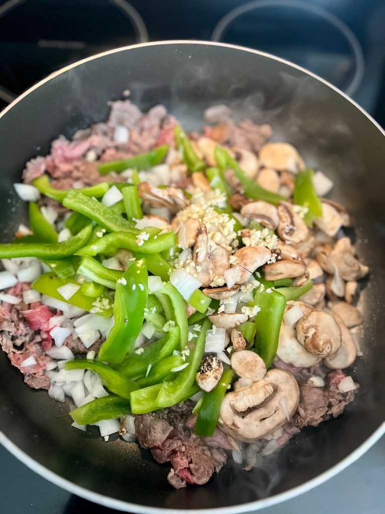 A large skillet filled with steak, pepper, onion, garlic, mushrooms, and seasonings