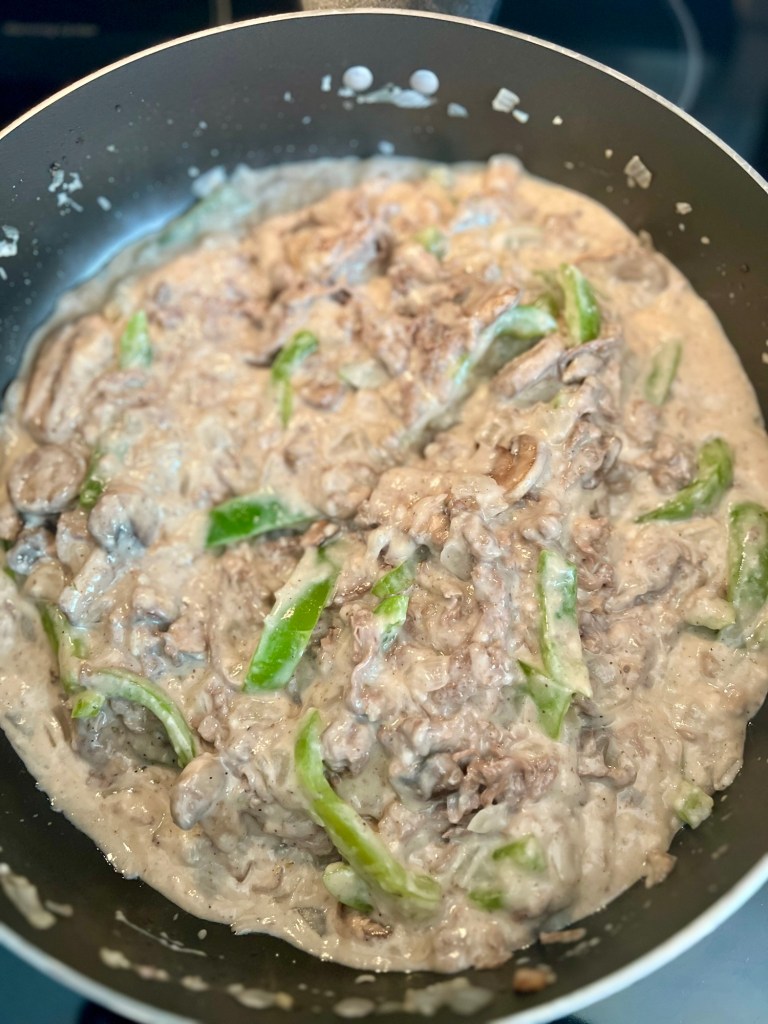 All the filling ingredients for Philly Cheesesteak Casserole in a large skillet ready to go into a pan