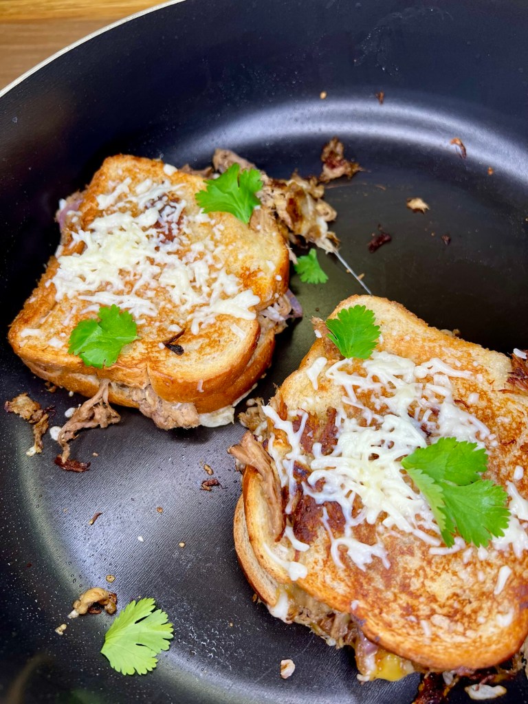Pulled Pork Grilled Cheese sandwiches with cheese and cilantro on top in a skillet on the stove