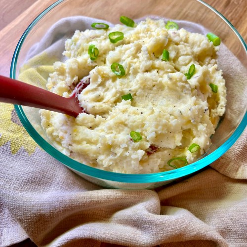 Creamy mashed potatoes in a glass dish with green onion on top and a red serving spoon inside