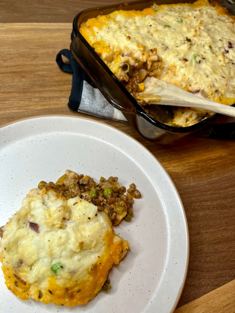 Shepard's pie in a large baking dish with a helping scooped onto a white plate in front of it