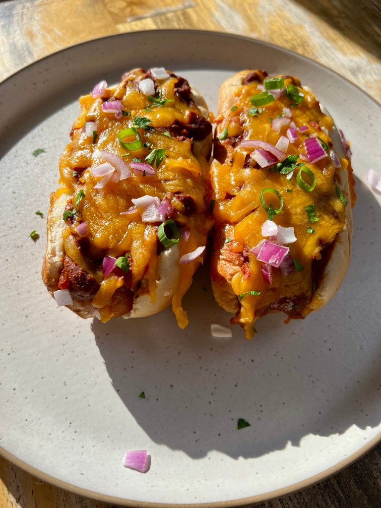 Chili cheese dogs on a white plate on a wooden table