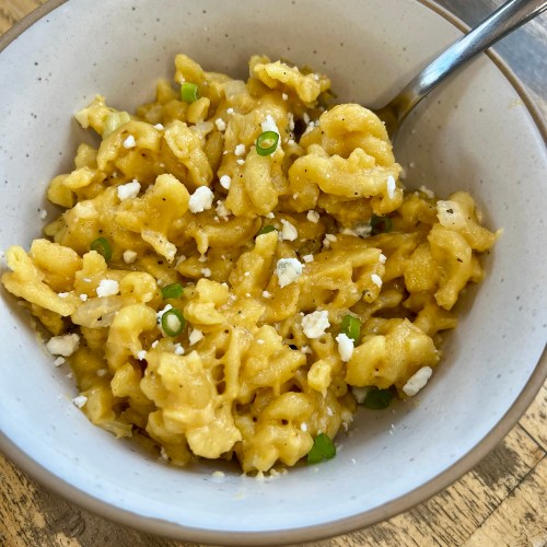 Crockpot mac and cheese in a white bowl with a spoon inside, on a wooden table