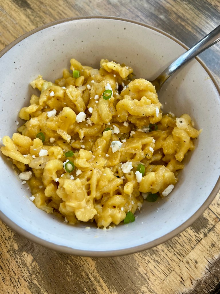 Crockpot mac and cheese in a white bowl with a spoon inside, on a wooden table