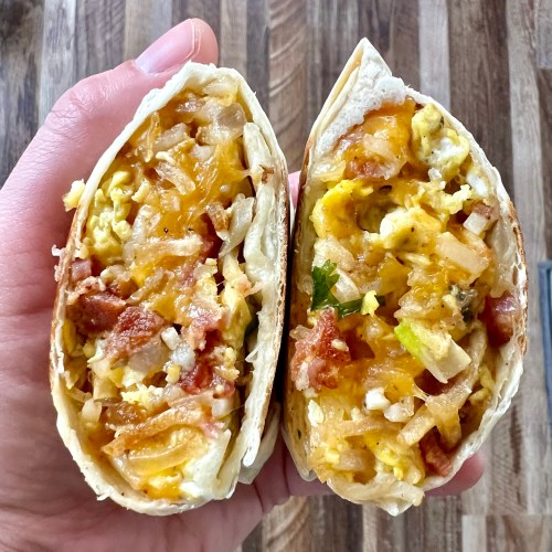 A breakfast burrito that's been cut in half and a hand is holding it to show the inside