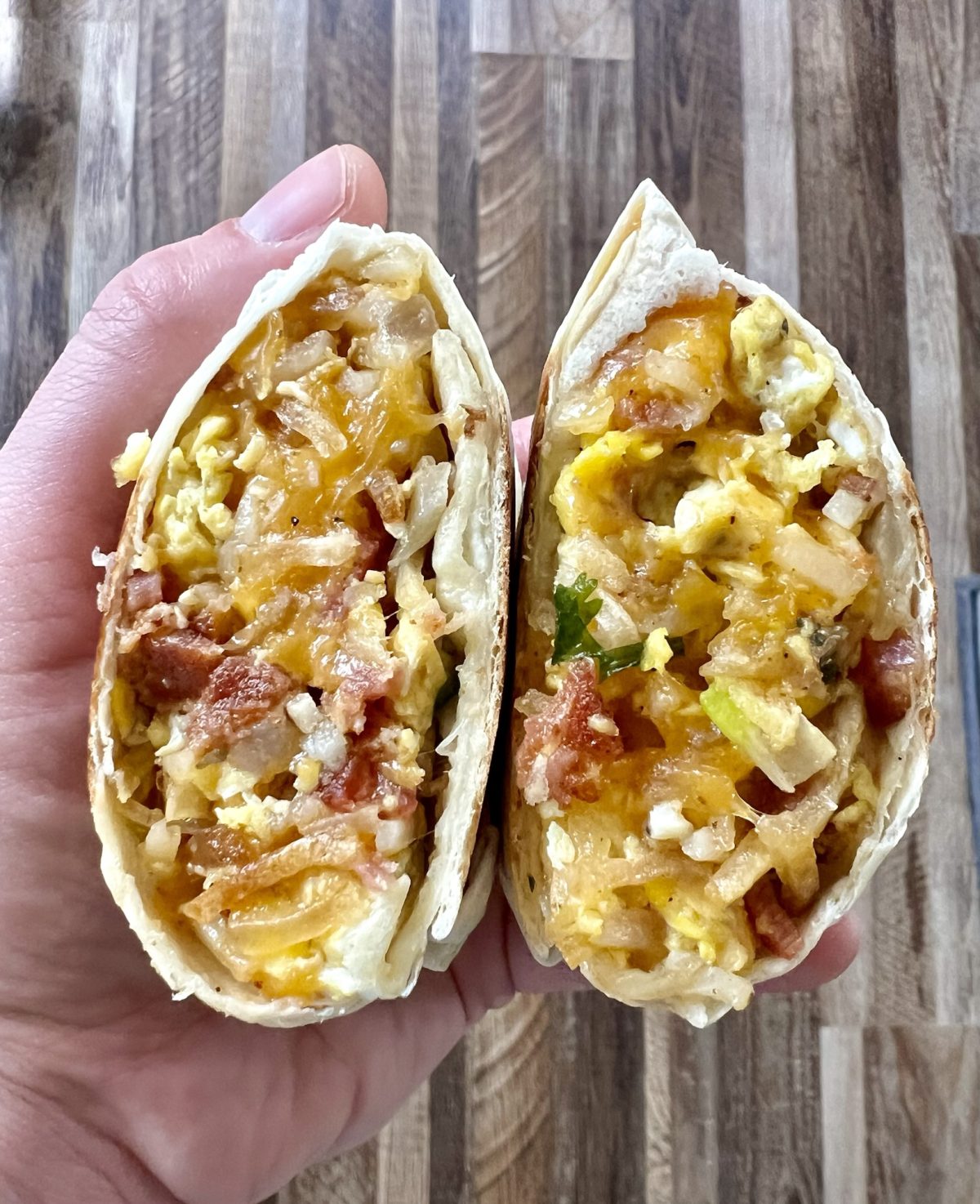 A breakfast burrito that's been cut in half and a hand is holding it to show the inside