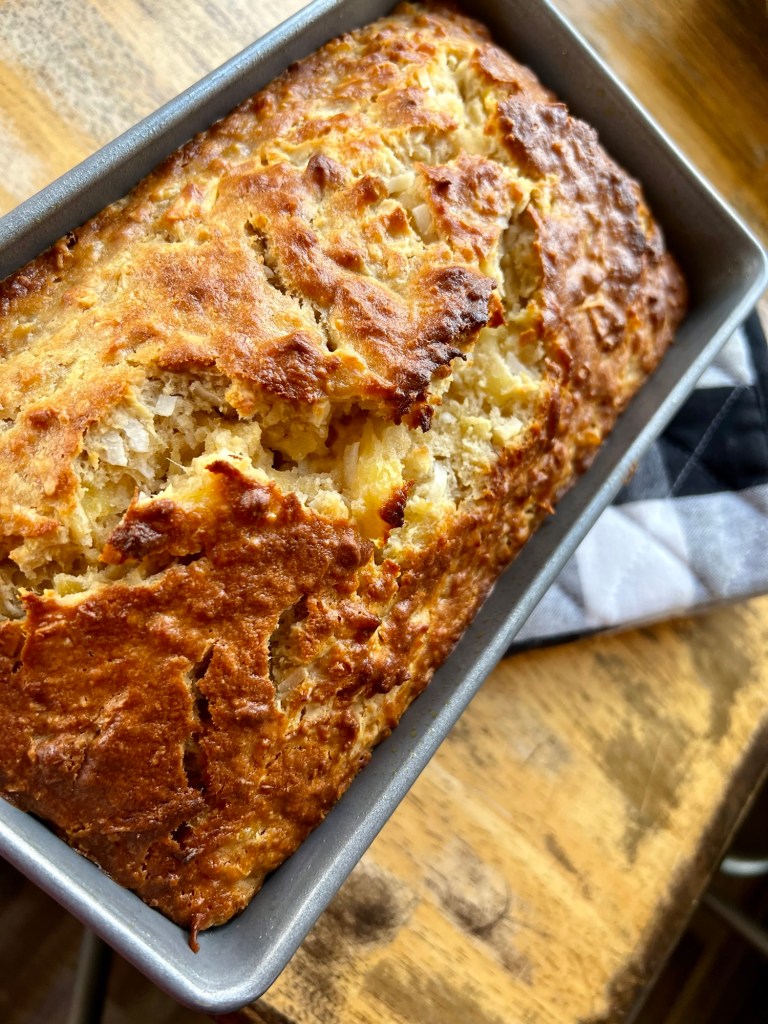 Tropical Banana Bread in a loaf pan on a hot pad, sitting on a wooden table