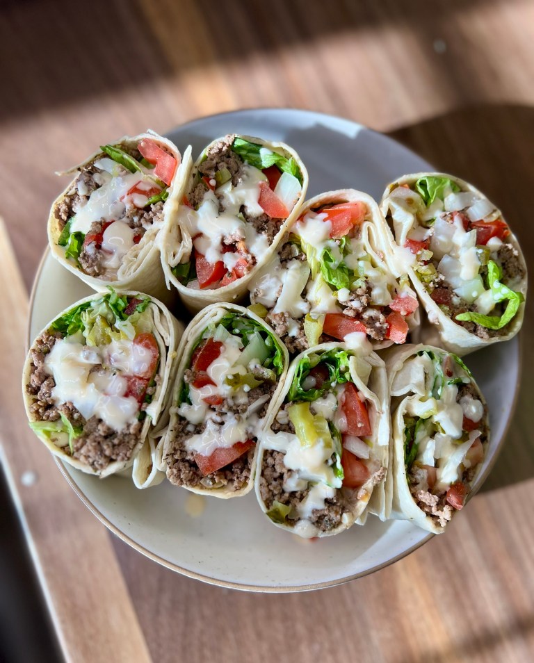 Beer cheeseburger wraps sliced in half on a white plate on a wooden countertop