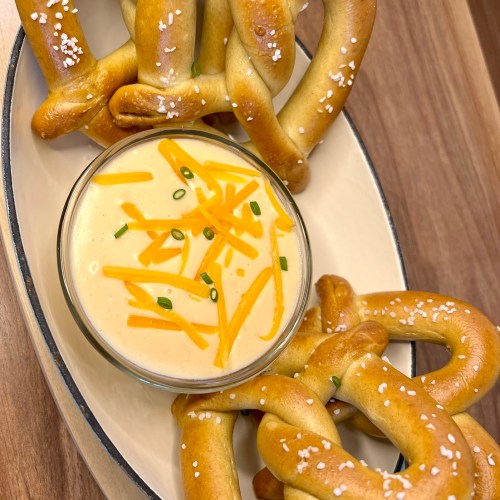 Beer cheese served with some pretzels in a serving dish on a wooden counter