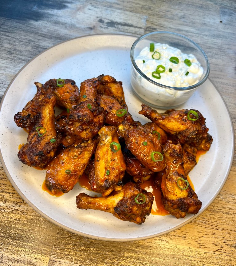 Hot wings on a white plate with blue cheese dressing in a dish next to it
