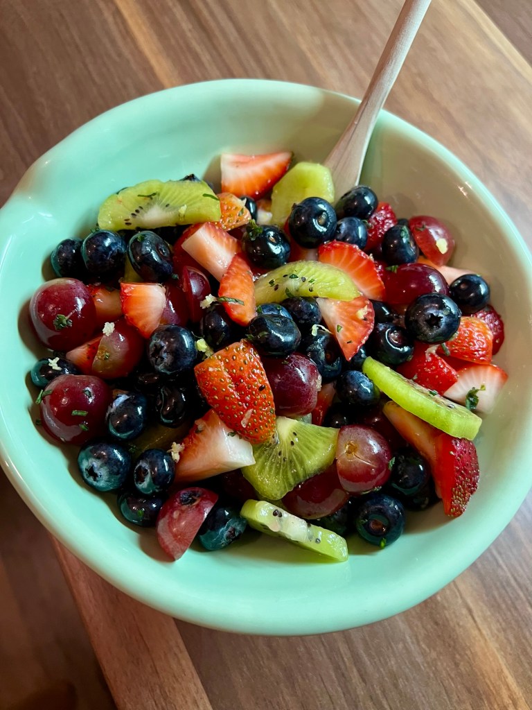 Fruit Salad in a blue bowl with a wooden spoon inside, on a wooden table