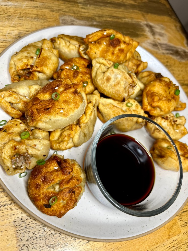 Chinese dumplings on a white plate with a small dish of soy sauce next to it