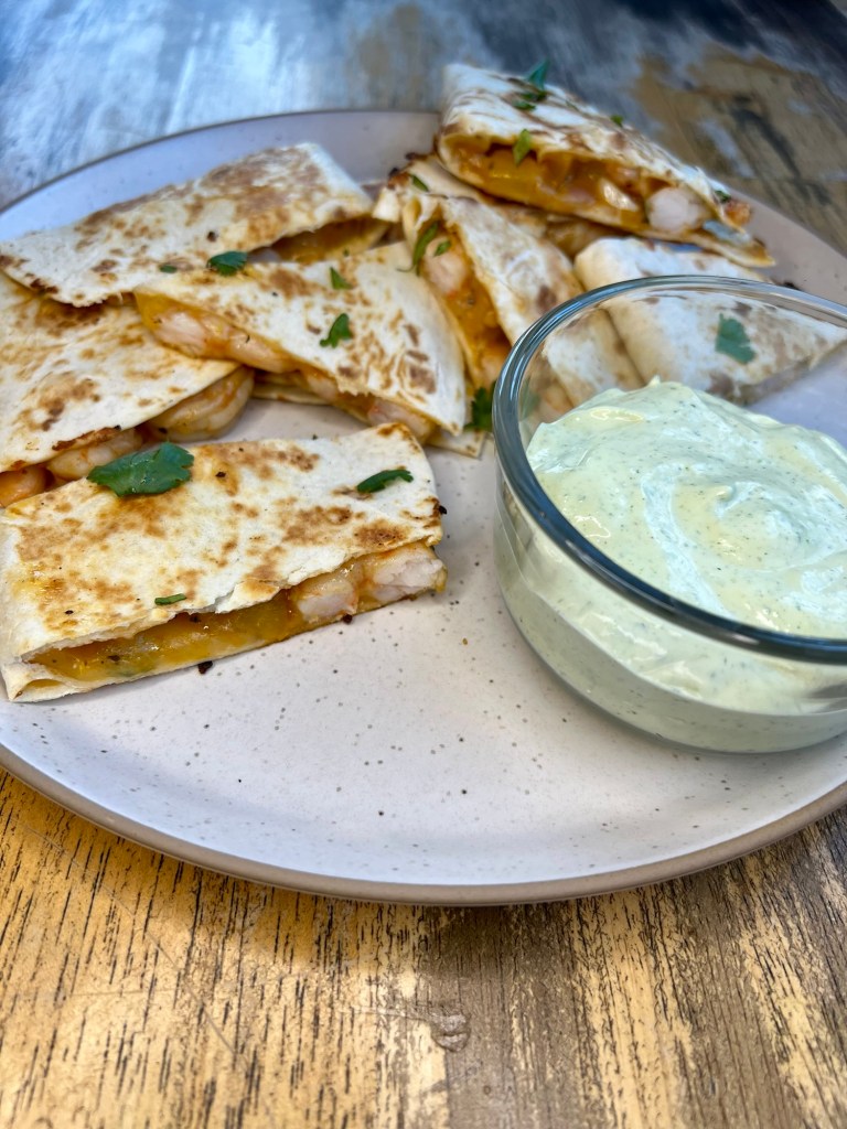 Shrimp quesadillas on a white plate with a side of cilantro lime crema next to it
