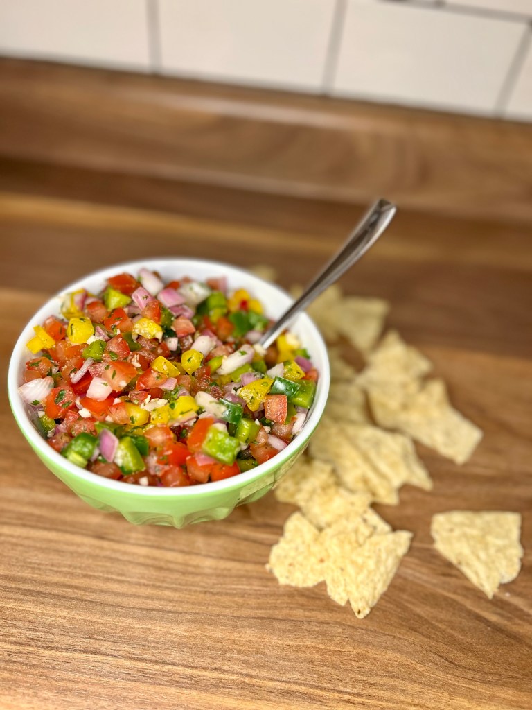 Homemade salsa in a green bowl with a spoon sticking out of it and some chips scattered around
