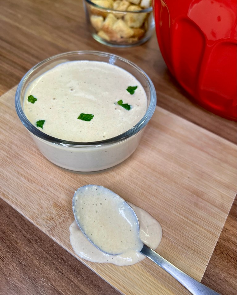 Caesar dressing in a small glass dish on a wooden cutting board with a spoonful of it nearby