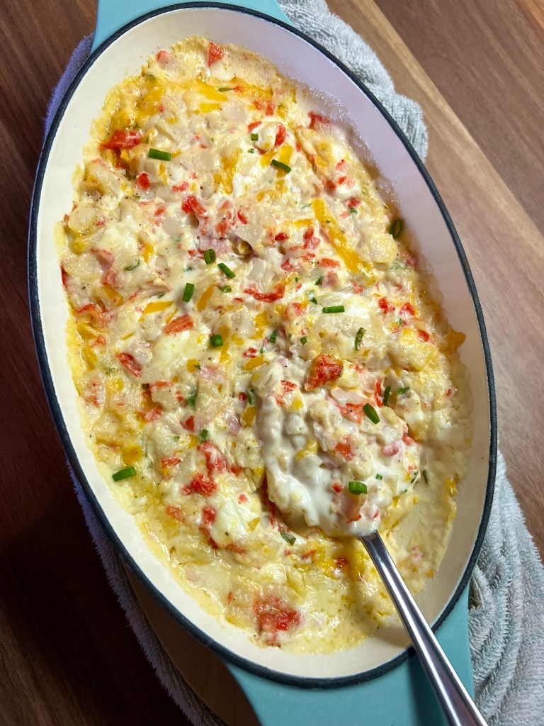Hot crab dip in a baking dish with a spoon inside on a wooden counter