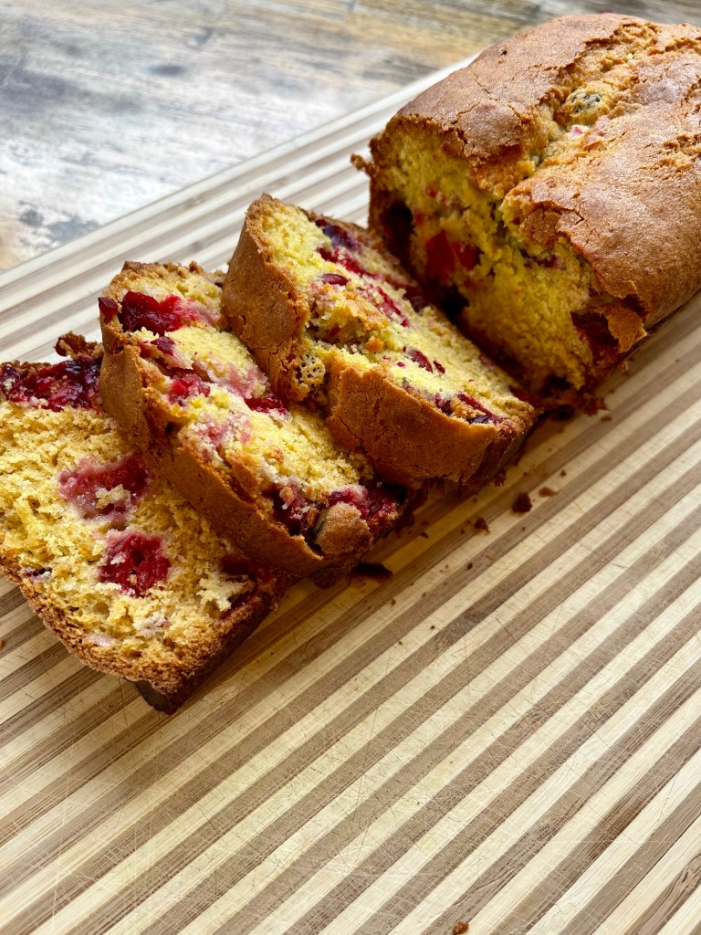 A cranberry orange bread loaf that's been sliced, on a wooden cutting board