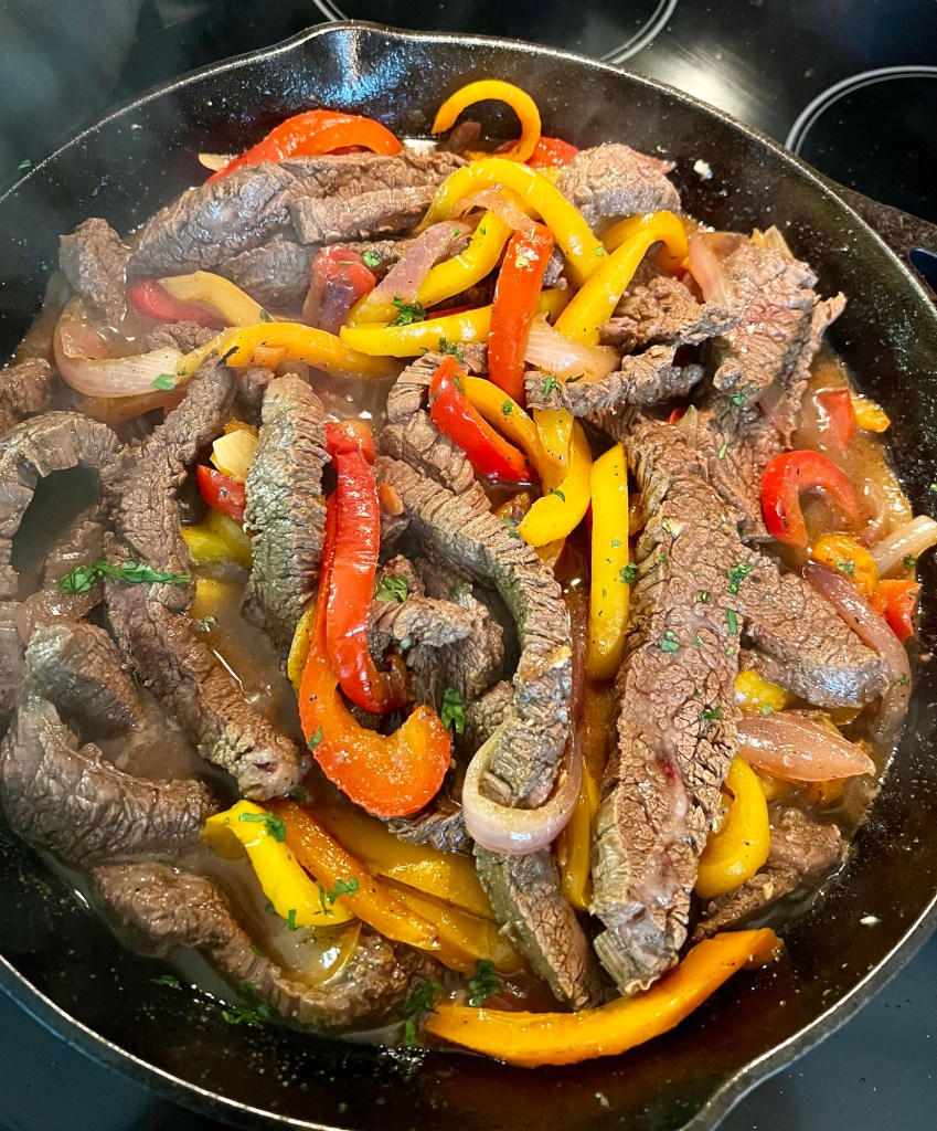 SRF Steak, peppers, and onions cooking in a cast iron skillet on the stove
