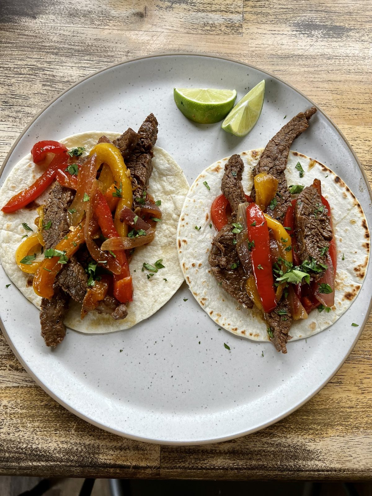 Flank Steak Fajitas on a white plate on a wooden table