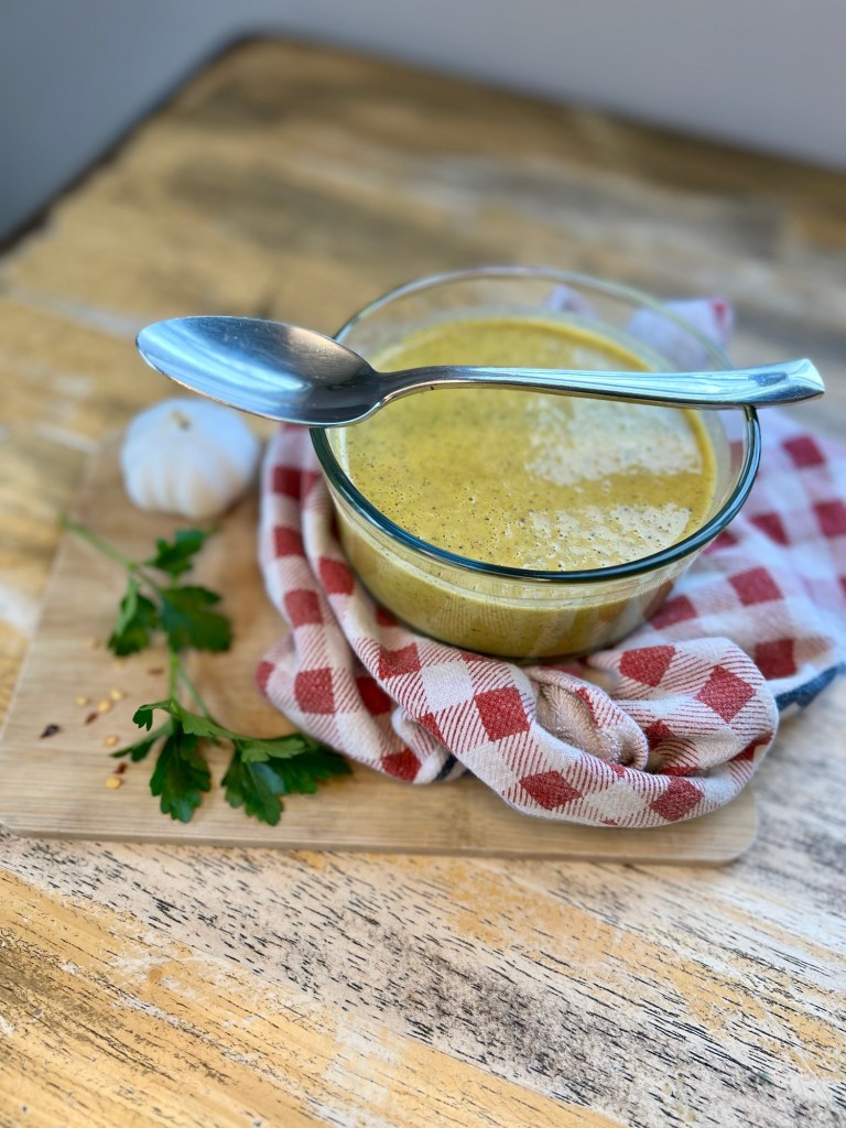 Homemade Italian Dressing in a dish with herbs and garlic next to it, on a table