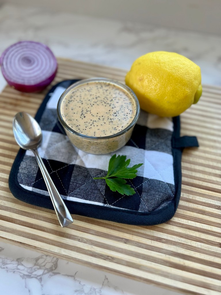 Lemon Poppy Seed Dressing in a ramekin on a hot pad with some lemon and onion next to it