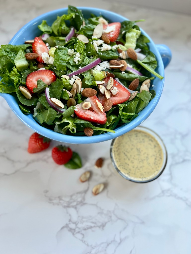 Strawberry Salad with onion, almond, and dressing next to it on a marble counter
