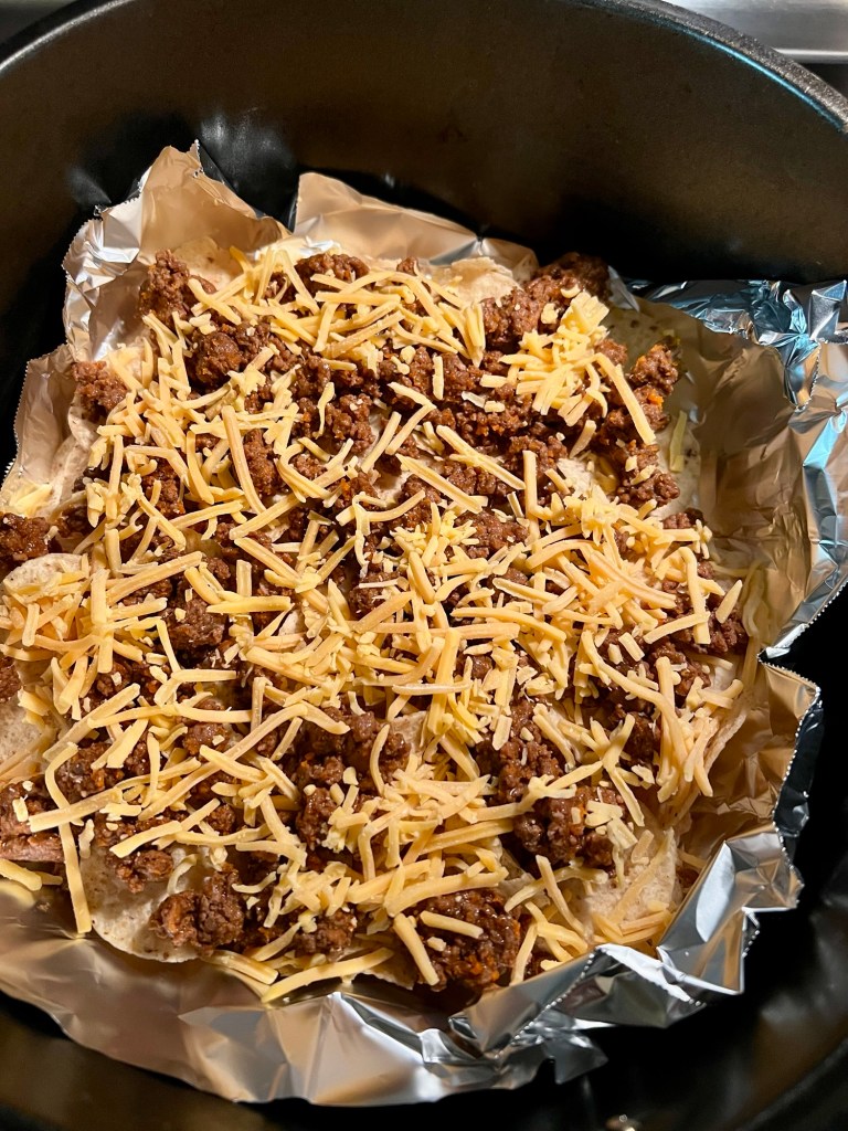 Tortilla chips, cheese, and taco meat in an air fryer basket to make nachos