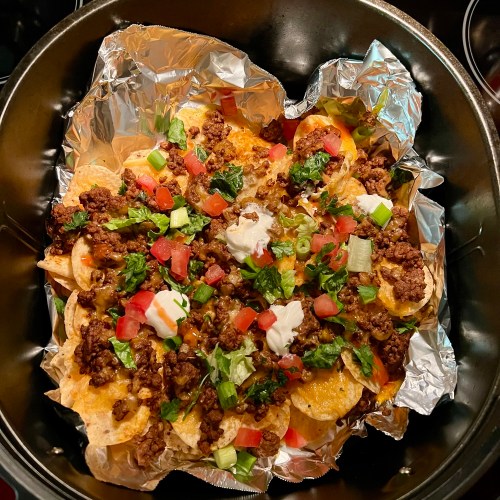 Air fryer nachos with garnishes on top in an air fryer basket