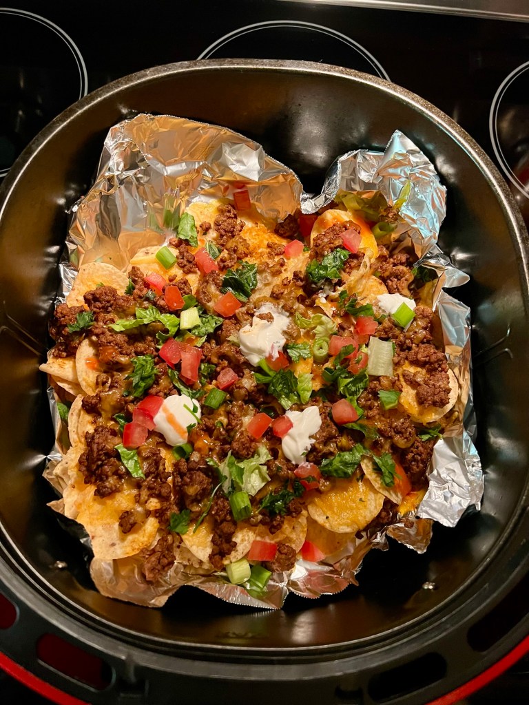 Air fryer nachos with garnishes on top in an air fryer basket