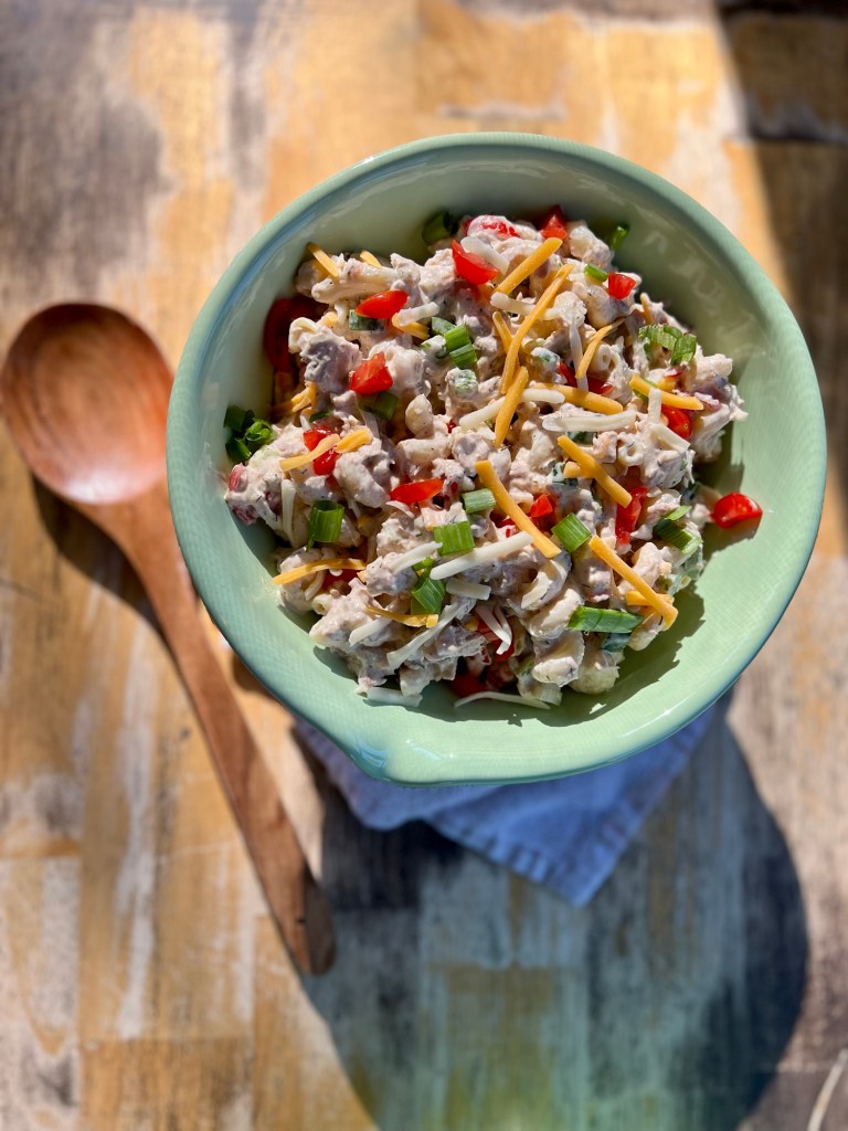 Spicy Tuna Pasta Salad in a large green bowl with a wooden spoon next to it on a wooden table